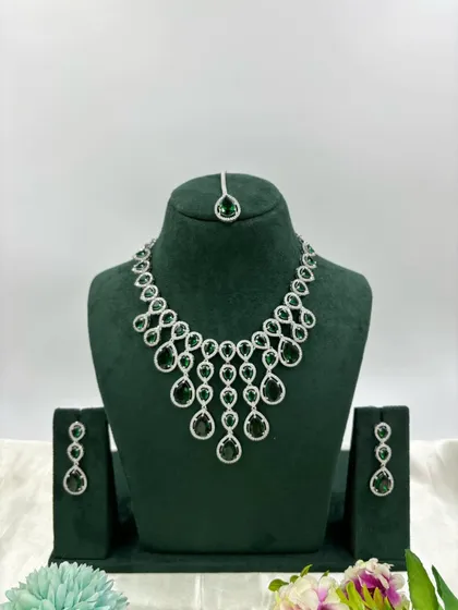 A delicate AD necklace with hanging green stones and a matching maang tikka.