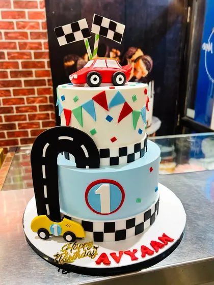 A two-tier race car cake for a first birthday, with a checkered flag pattern and a winding road for the cars.