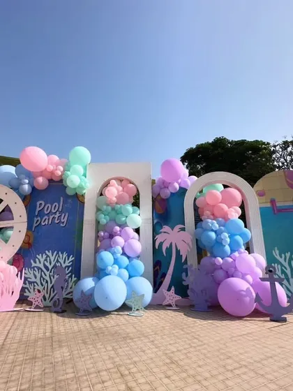 A wide view of the poolside party setup, showing how different elements come together. The custom backdrops, ship's wheel prop, and cascading pastel balloons create a cohesive and immersive environment for the celebration.