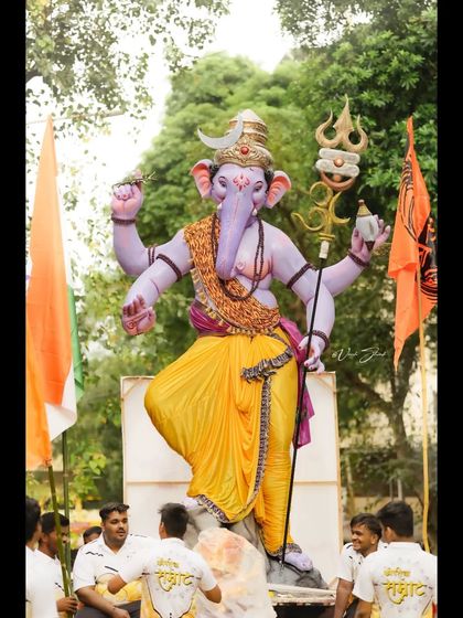 A full view of the Kopri Cha Samrat idol during the day, surrounded by lush greenery and devotees.