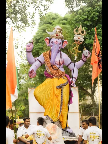 A full view of the Kopri Cha Samrat idol during the day, surrounded by lush greenery and devotees.