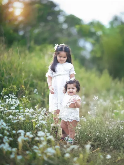 Two sisters standing together in a field of white flowers. The bond between them is so sweet and clear.