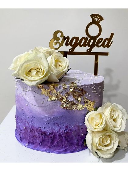 An engagement cake with a beautiful purple ombre texture. It's decorated with white roses and gold leaf for a touch of elegance.