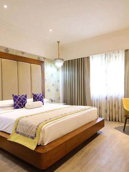 A clearer, full shot of the Vivanta Bengaluru room. The design combines a custom damask-style wallpaper with a modern wooden bed frame and pops of purple in the cushions, creating a look of understated luxury.