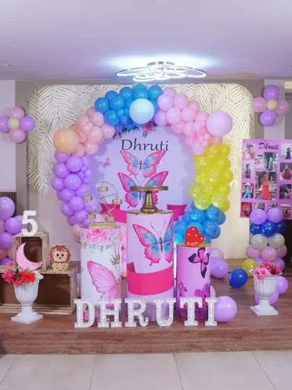 A full view of this vibrant butterfly theme for a 5th birthday party. The setup includes a custom circular backdrop, themed pedestals, and a colorful balloon arch.