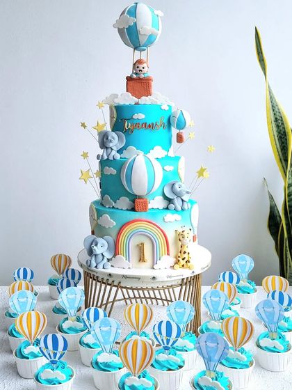 A grand four-tiered hot air balloon cake with matching cupcakes. This cake is perfect for a big celebration and features cute animals in the balloons.