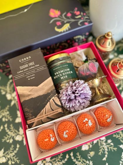 A detailed view of our pink Diwali box, perfect for those who prefer sugar-free options. It includes Carra sugar-free chocolate along with festive essentials like ladoo candles, a brass diya, and a premium nut mix.