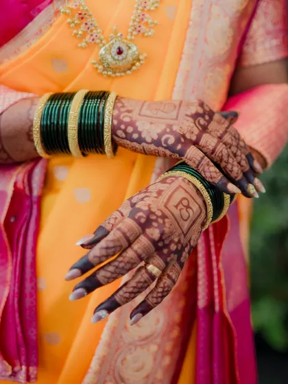 The intricate details of a bride's attire are part of her story. This shot highlights the beautiful bridal mehndi design, featuring the couple's initials, and the traditional green glass bangles worn by Maharashtrian brides.