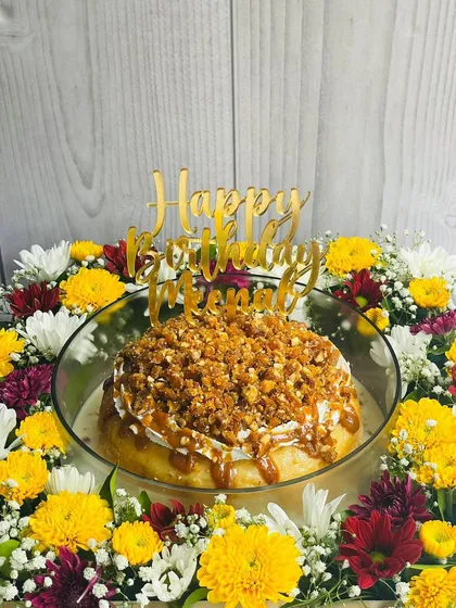 The Butterscotch Caramel Tres Leches sits beautifully within a floral arrangement, making it a stunning and delicious centerpiece for a birthday party.