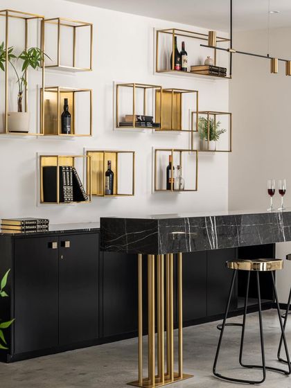 This bar in the Ebony & Ivory project is the epitome of moody sophistication. A black marble waterfall countertop is supported by a sculptural brass base, with floating brass box shelves for a minimalist yet glamorous display.