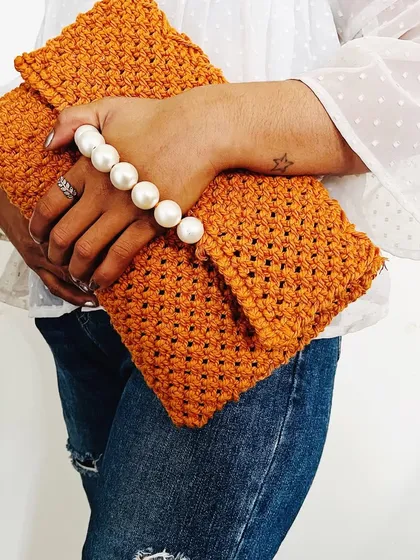 A different way to hold the macramé clutch, showcasing its soft, foldable texture. The pearl handle adds a touch of elegance, making it suitable for both ethnic and western wear.