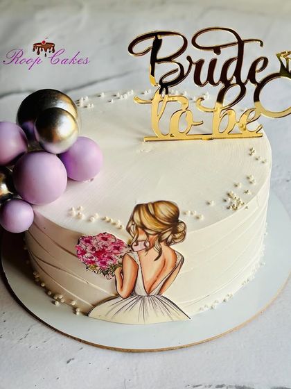 A chic and elegant cake for a bride-to-be. This design features an edible illustration of a bride, complemented by lavender and silver balloon decorations and a golden topper.