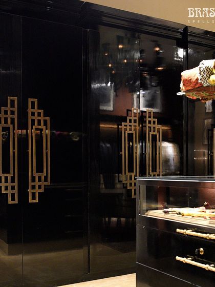 Set against glossy black wardrobes, the brass handles create a dramatic, high-contrast look. The reflection in the doors adds depth, making the hardware a captivating focal point within the designer's opulent retail space.