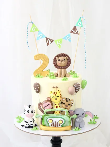 A delightful jungle safari cake perfect for a child's second birthday. This design is packed with fun, featuring adorable, handmade fondant animals like a lion, zebra, and monkey, all ready for a jeep adventure.
