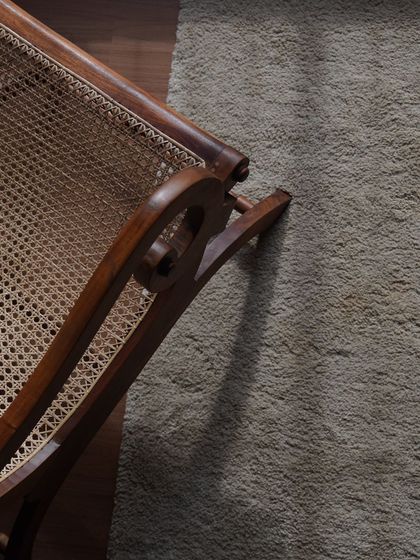 An overhead detail of the planter's chair, highlighting the hand-caned seat and the unique, curved shape of the teak armrest.