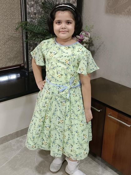 A happy girl posing in her light green floral dress. The flutter sleeves and simple tie-belt make this a comfortable and charming choice for everyday wear.