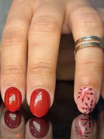 A festive red manicure with a pink accent nail featuring a shiny red snowflake design.