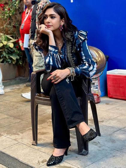 A candid shot of Mrunal between takes, showcasing one of Rabia's signature looks. The tie-dye blouse with ruffled shoulders is paired with an embroidered waistcoat and accessorized with stacked silver bangles and custom mirror-work mules, defining her eclectic fashion sense.