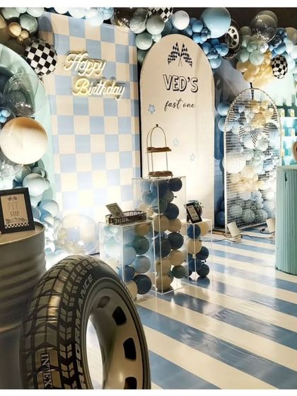A "Ved's Fast One" race car party with a blue and white checkerboard theme. The decor includes tire props, a neon sign, and striped flooring to complete the racetrack look.