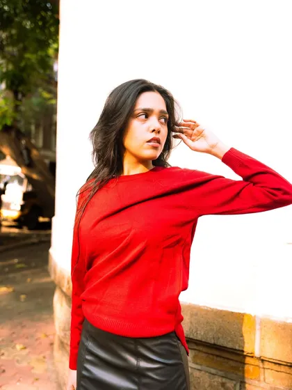 Using a simple white wall to make the bright red sweater pop. This is a great example of using color contrast in a portrait.