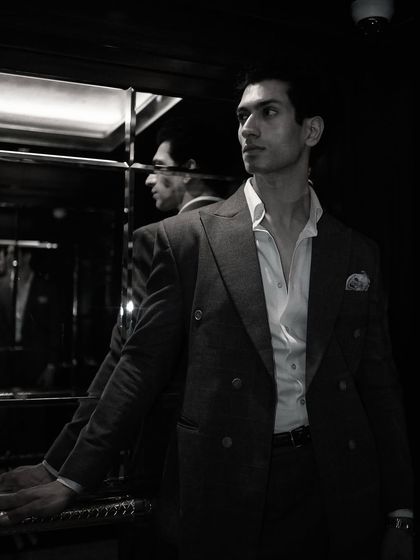 A moody, atmospheric shot of our client in his double-breasted suit. The reflections emphasize the suit's sharp silhouette and the wearer's confident presence.