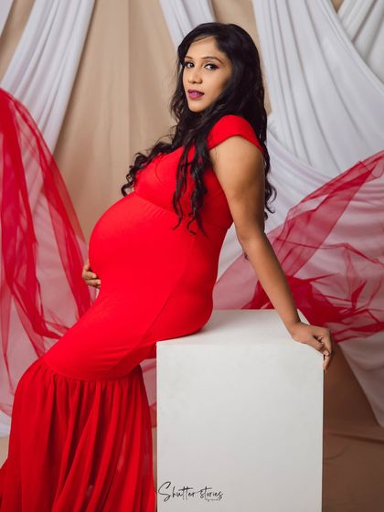 Slaying in bold red. This studio shot showcases a powerful and confident pose, with the vibrant red dress beautifully highlighting the baby bump against a simple, elegant backdrop.