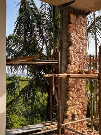 A detail of the coral stone work at Kizikula, with a view out to the ocean and palm trees. The texture of the stone contrasts beautifully with the lush landscape, grounding the building in its tropical setting.