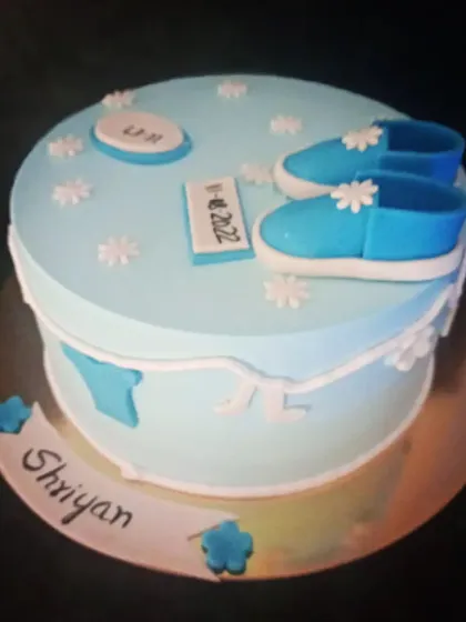 A lovely blue cake for a baby's naming ceremony. It's decorated with tiny shoes and flowers, and includes a plaque with the baby's name and date.