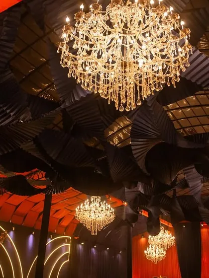 An upward-looking shot of the ceiling, highlighting the contrast between the industrial-style black fans and the classic elegance of the crystal chandeliers.