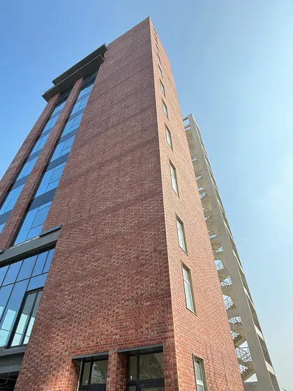 An upward view of a recently completed office building, capturing the powerful interplay between the solid, earthy texture of exposed brick and the sleek, reflective quality of a modern glass curtain wall.