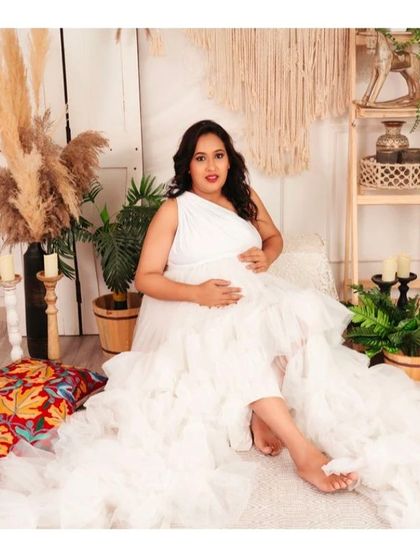 A beautiful portrait of a mom-to-be in our white one-shoulder ruffled gown, set in a bohemian studio.