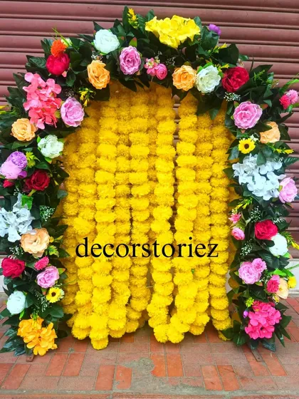 A vibrant and traditional ready-to-install makhar, perfect for Haldi ceremonies or Ganpati festival decor. This backdrop features dense yellow marigold garlands framed by a colorful arch of artificial roses, creating a classic festive look.