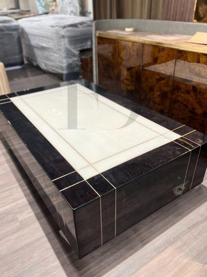 This center table combines a dark, high-gloss veneer with a central white onyx panel and delicate brass inlay. The design is a perfect example of modern luxury, blending different materials for a sophisticated result.
