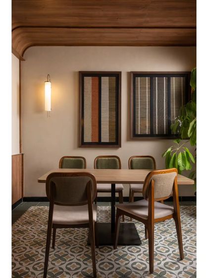 A cozy dining setup for four, featuring patterned floor tiles and framed textile art. The warm, focused lighting from the wall sconce makes this a perfect spot for an intimate meal.