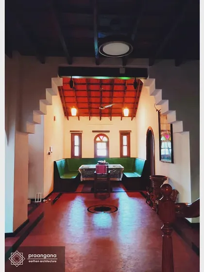 This is the heart of our Udupi residence project, a space that flows under a corbelled arch. The glossy red oxide floor reflects the light, contrasting beautifully with the cool white lime-plastered walls and the warm tones of the wooden ceiling beams.