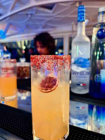 A close-up of a stunning cocktail with a chili-dusted rim and a dehydrated lime garnish. The layers of flavor and texture make this a truly special drink.