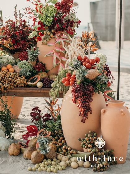 A lush installation of tropical fruits and flowers on the beach in Goa. The arrangement includes pineapples, papayas, grapes, and vibrant blooms, creating a feast for the eyes.