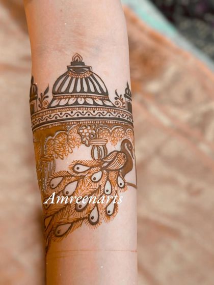 A close-up of an arm band with a peacock looking out from a palace window.