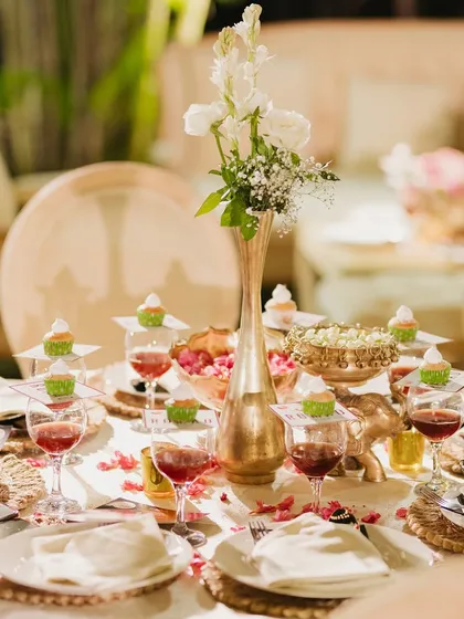 An exquisite table setting for a 75th anniversary dinner. The elegant white and gold theme is complemented by delicate floral centerpieces and individual cupcakes for each guest.