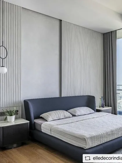 The master bedroom continues the minimalist theme with a combination of concrete texture and fluted panels behind the bed. The design creates a calm and restful atmosphere, with large windows offering expansive city views.