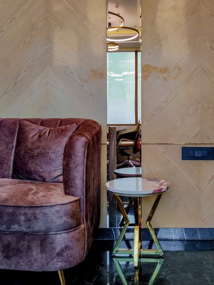 A detail shot showing the material interplay in an office cabin: plush velvet, a marble-topped side table with a gold base, and chevron-patterned wood veneer. This combination of textures adds depth and luxury.