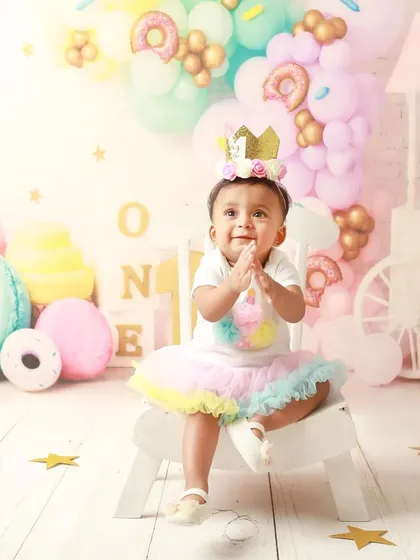 The birthday girl, wearing her crown, claps her hands in delight during her donut-themed party shoot.