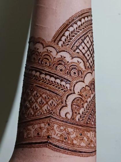 A detailed shot of an intricate henna band on the forearm. This design uses layers of patterns, including swirls and grids, to create a rich texture.