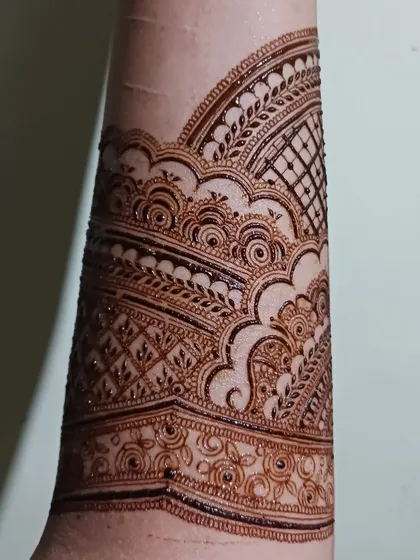 A detailed shot of an intricate henna band on the forearm. This design uses layers of patterns, including swirls and grids, to create a rich texture.