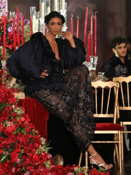 A model poses on the banquet table runway for Siddartha Tytler's show. The set itself became a part of the performance, with a cascade of red flowers creating a powerful contrast against the dark, moody couture.