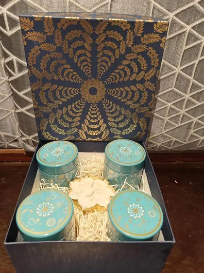 This luxury hamper features a deep blue and gold box filled with four matching decorative tins and a floral-shaped diya.
