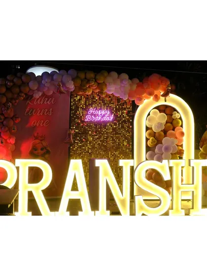 A glamorous princess party for Pranshi, featuring a stunning gold sequin backdrop, a "Happy Birthday" neon sign, and marquee letters, all set against a warm-toned balloon arch.