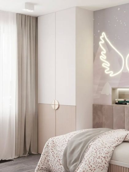 A serene and stylish kid's bedroom with a tufted headboard, a built-in reading niche, and a neon angel wings light feature. The wardrobe is a clean, two-tone design.