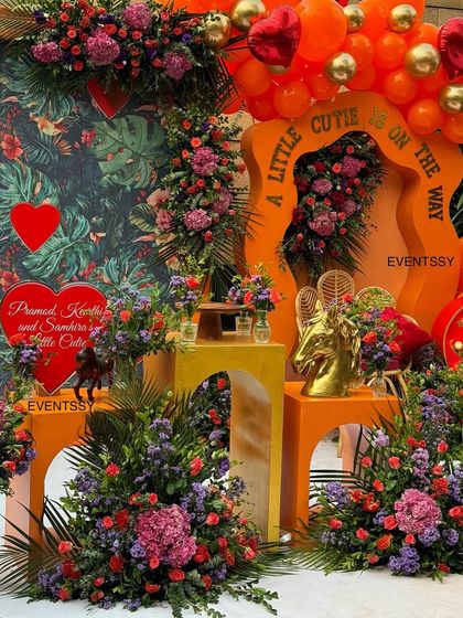 A closer view of the "Little Cutie" baby shower decor, highlighting the dense floral arrangements and the custom orange arch. The mix of bold colors and rich textures creates a warm and inviting atmosphere.