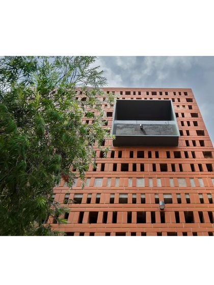A detail of the brick facade, showing the 'jaali' or screen work. A metal box window projects out from the screen, creating a small balcony for the kid's bedroom and adding a modern, industrial element to the traditional brickwork.